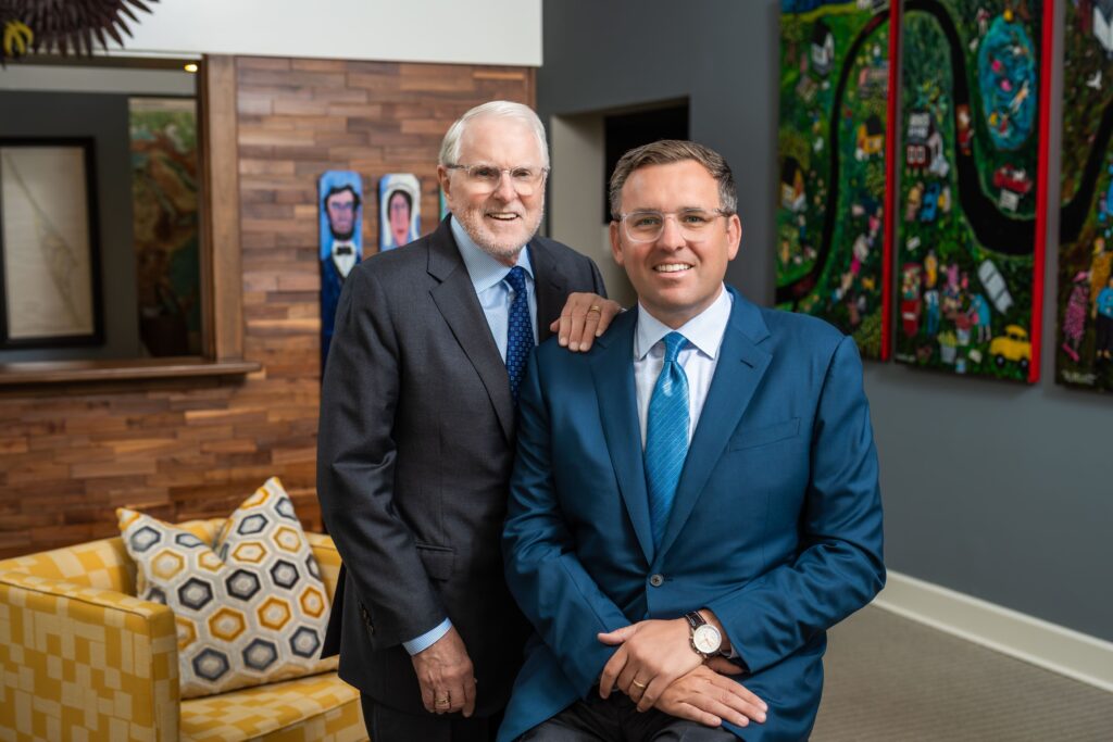 Jacob Stuart y Jacob Stuart Jr., fundadores de Jacob Stuart Law, compartiendo un momento de franqueza en la oficina de Orlando, vestidos con trajes azules y corbatas.