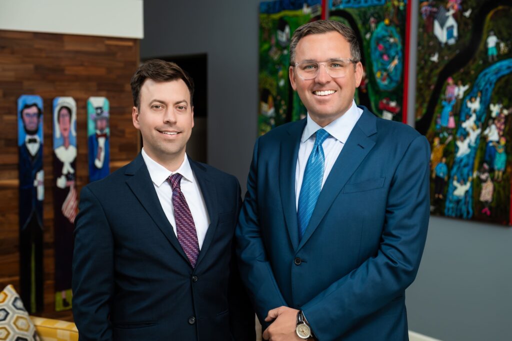Jacob Stuart Jr. and Ian Tudor, attorneys at Jacob Stuart Law in Orlando, Florida, standing together in the firm’s office wearing business suits
